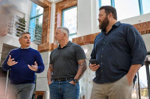 Three business partners walking together in a modern office building while engaged in conversation. One man gestures as he speaks while the others listen, illustrating collaboration, leadership, and strategic business planning. The image represents partnership, succession planning, and proactive decision-making in a professional business setting.