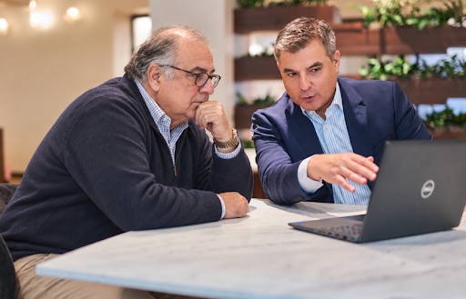 Two men reviewing information together on a laptop at a conference table, with one man pointing toward the screen while the other looks on thoughtfully.